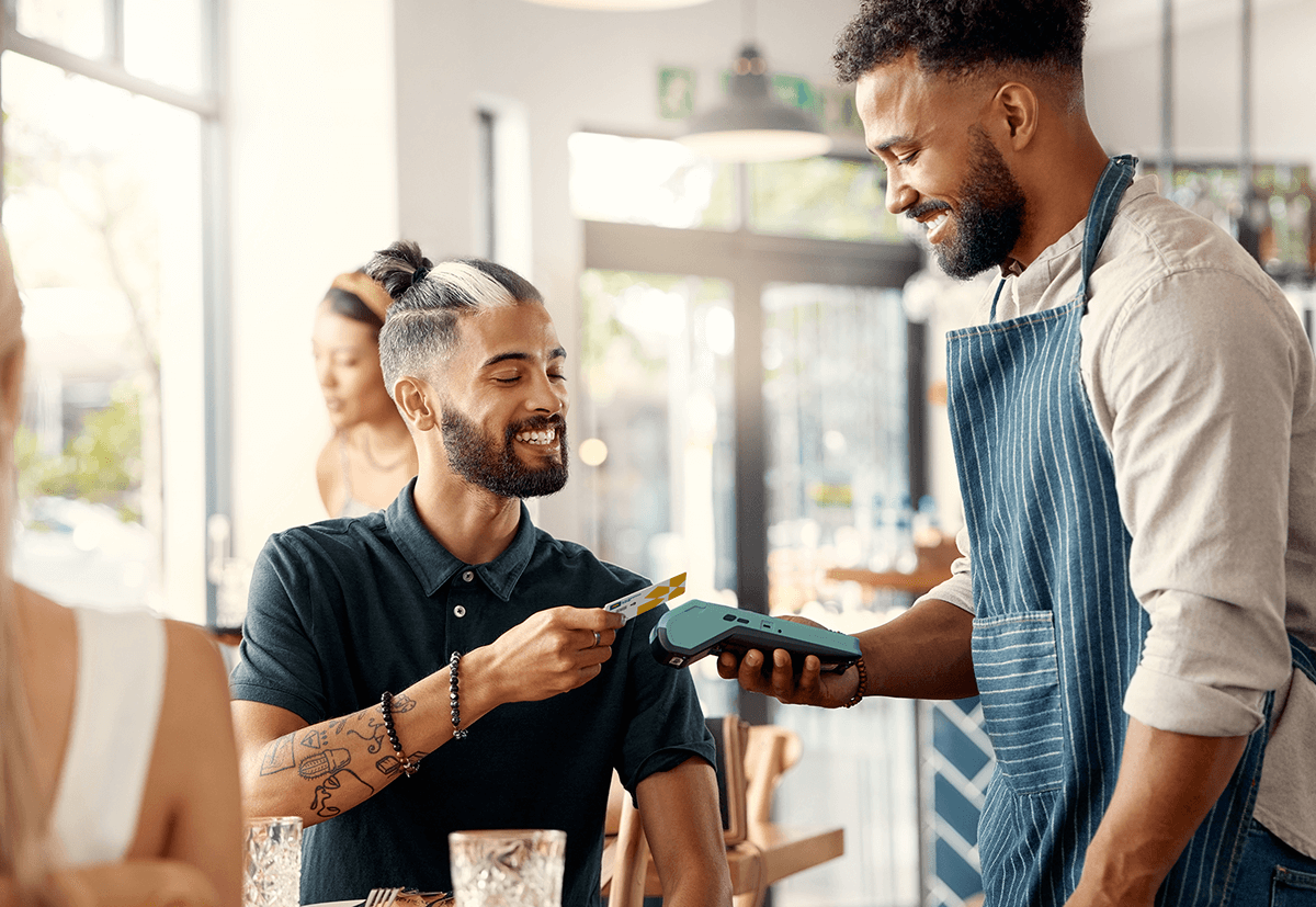 A man sitting in a restaurant pays for his meal by tapping his Laurentian Bank debit card on a wireless payment terminal held by the server.