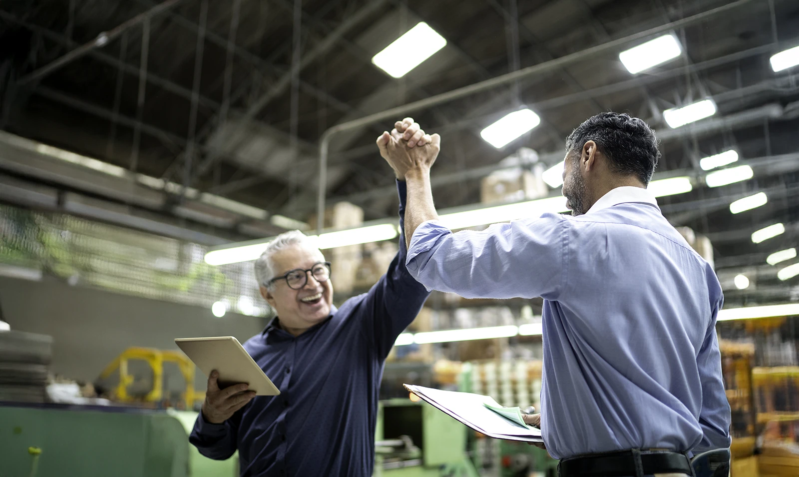 Deux travailleurs se tapent dans la main dans une usine tandis que d'autres applaudissent.