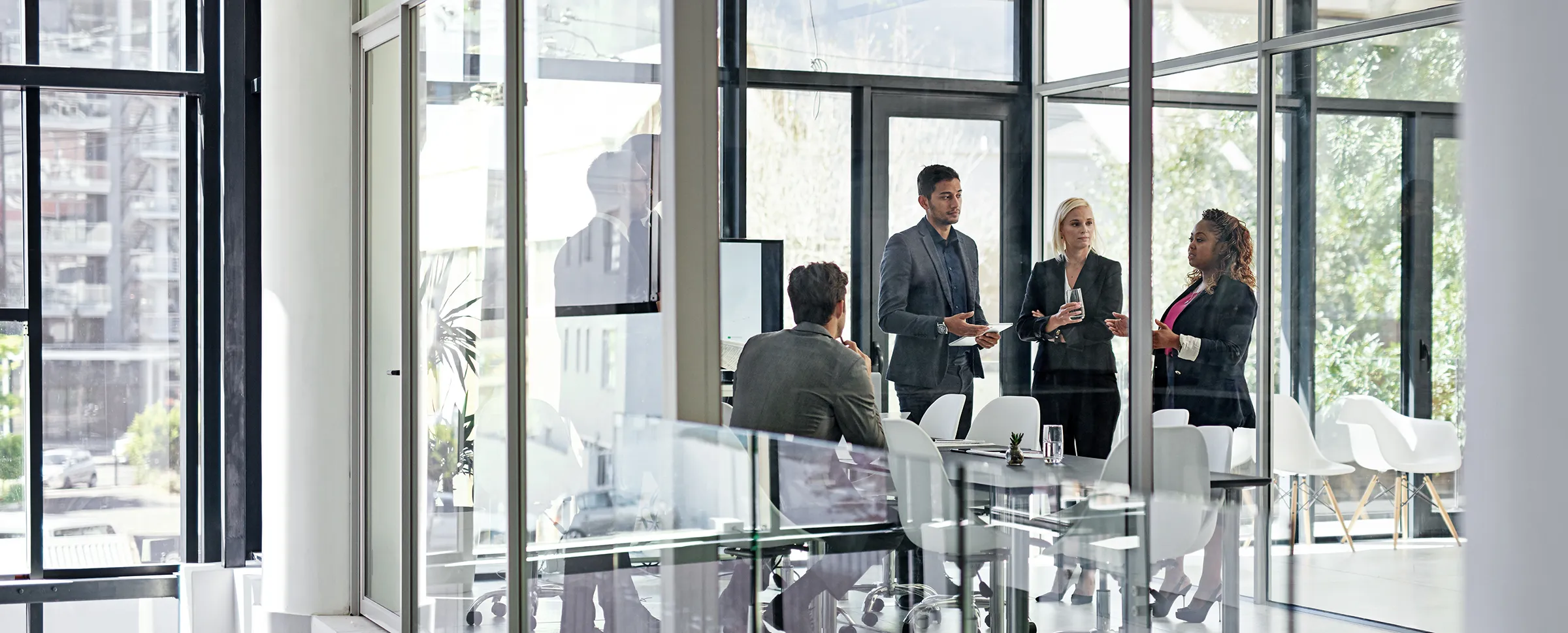 Un groupe de quatre professionnels discutent dans un bureau vitré. Une des quatre personnes est assise.