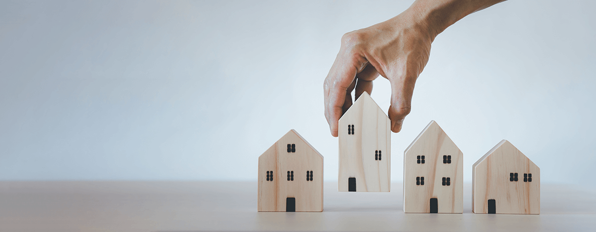 A close-up of a person’s hand placing a wooden house among other wooden houses.