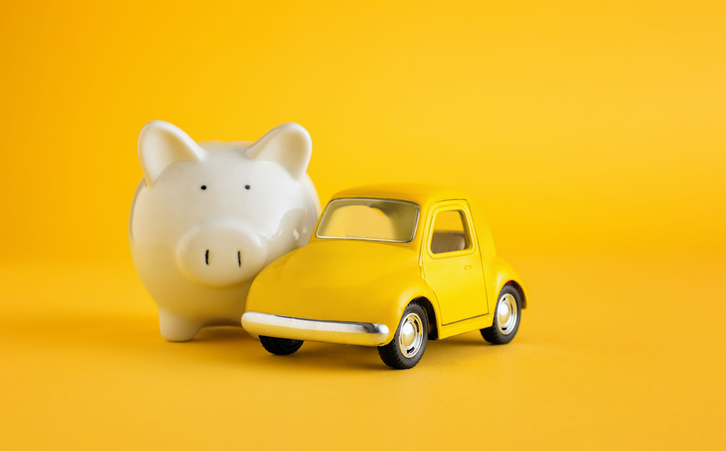  A white piggy bank beside a yellow toy car.