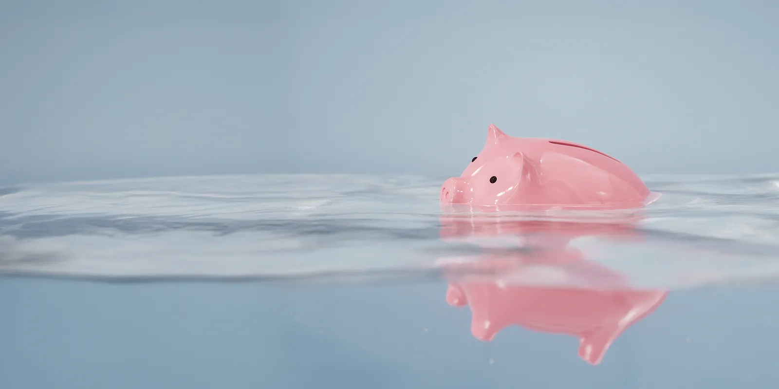 Une tirelire de couleur rose vif flotte dans l’eau, à moitié immergée.