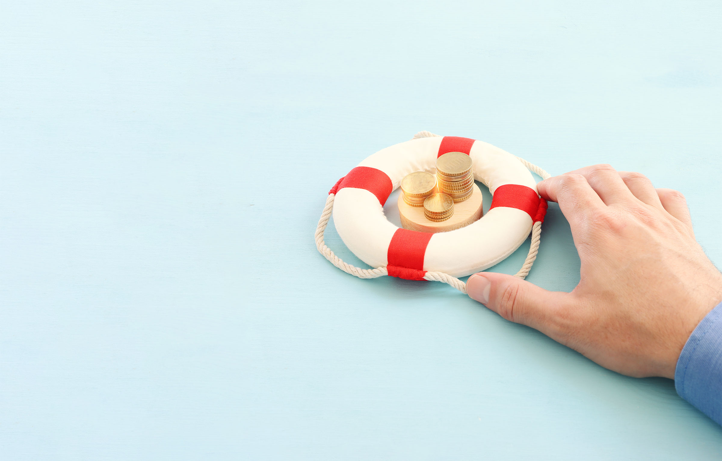 A man’s hand holds a tiny white and red striped life preserver that’s protecting a stack of coins.