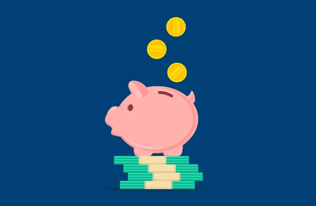 Gold coins fall into a piggy bank that sits on top of bill stacks.