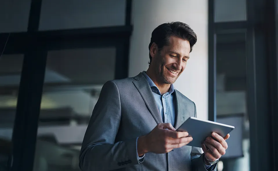 A man in a suit consults his tablet, smiling.