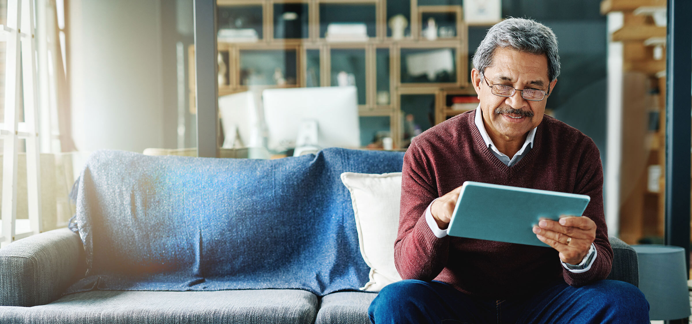 Un homme d'âge moyen est assis chez lui et utilise sa tablette.