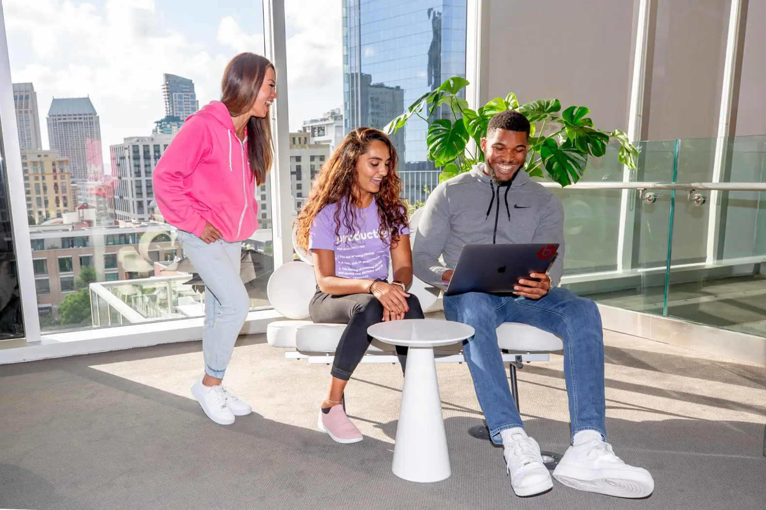 Three ClickUp employees in a common space gathered around a laptop.