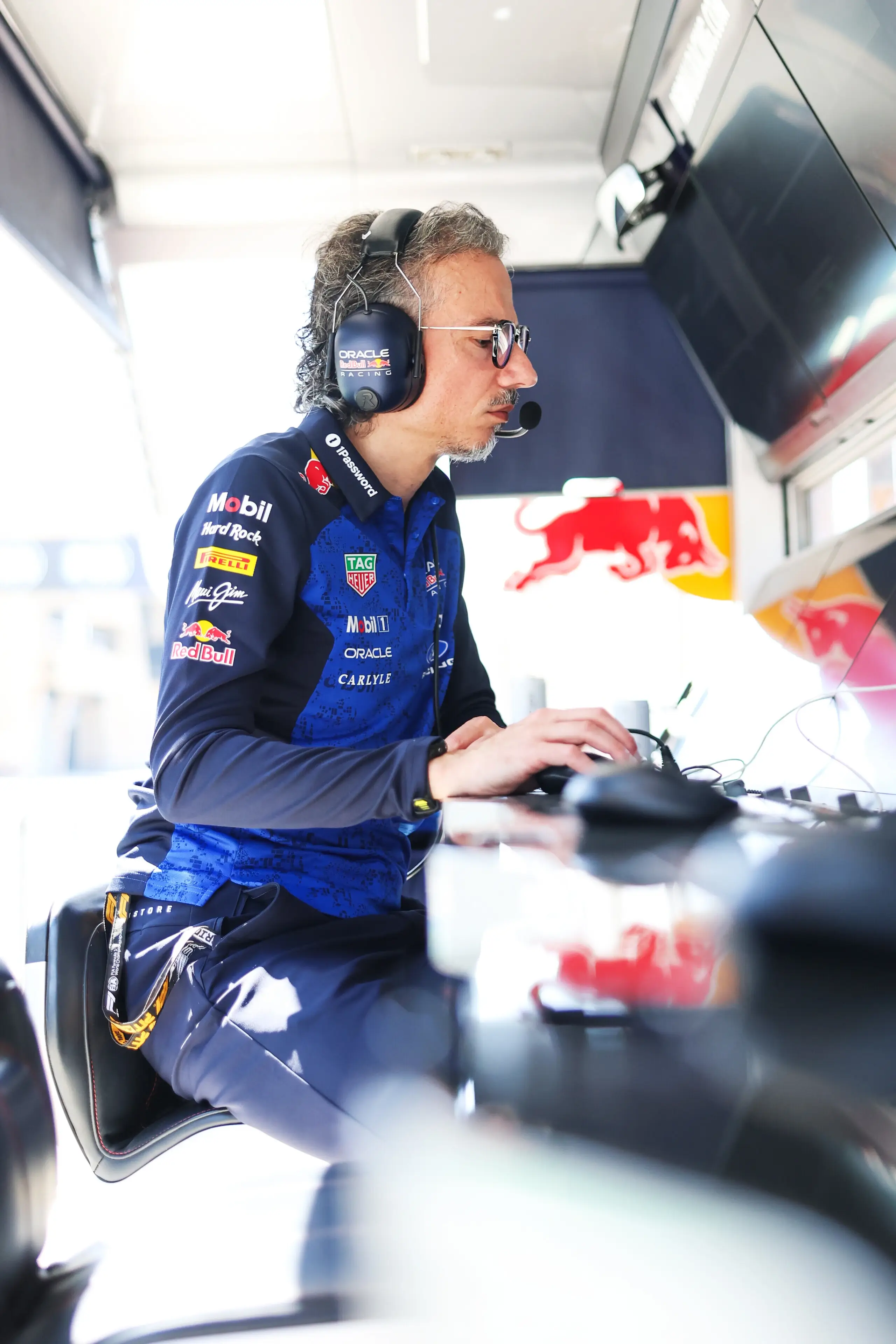 Oracle Red Bull Racing engineer wearing a headset works at a control station, looking at multiple screens inside the team garage.
