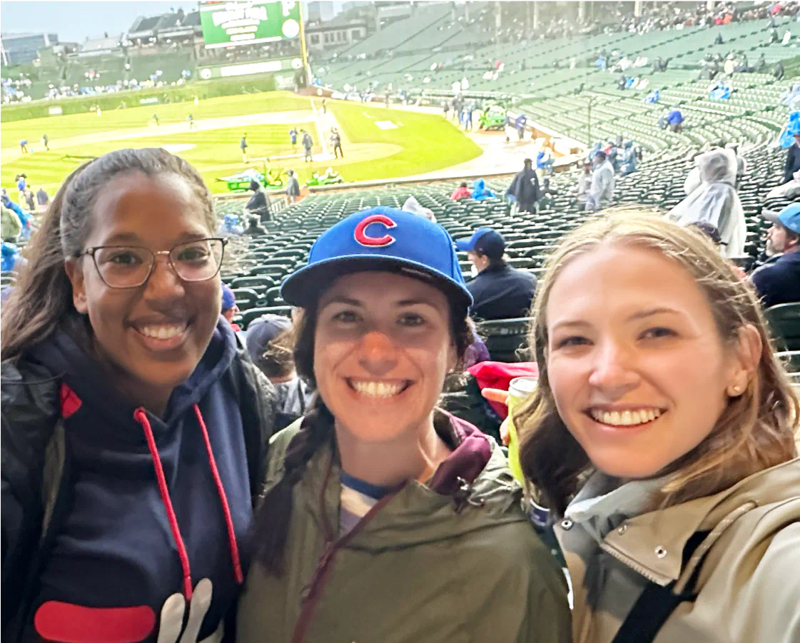 Tre donne felici a una partita di baseball, mentre si godono l'aspetto più sociale del loro lavoro presso 1Password.