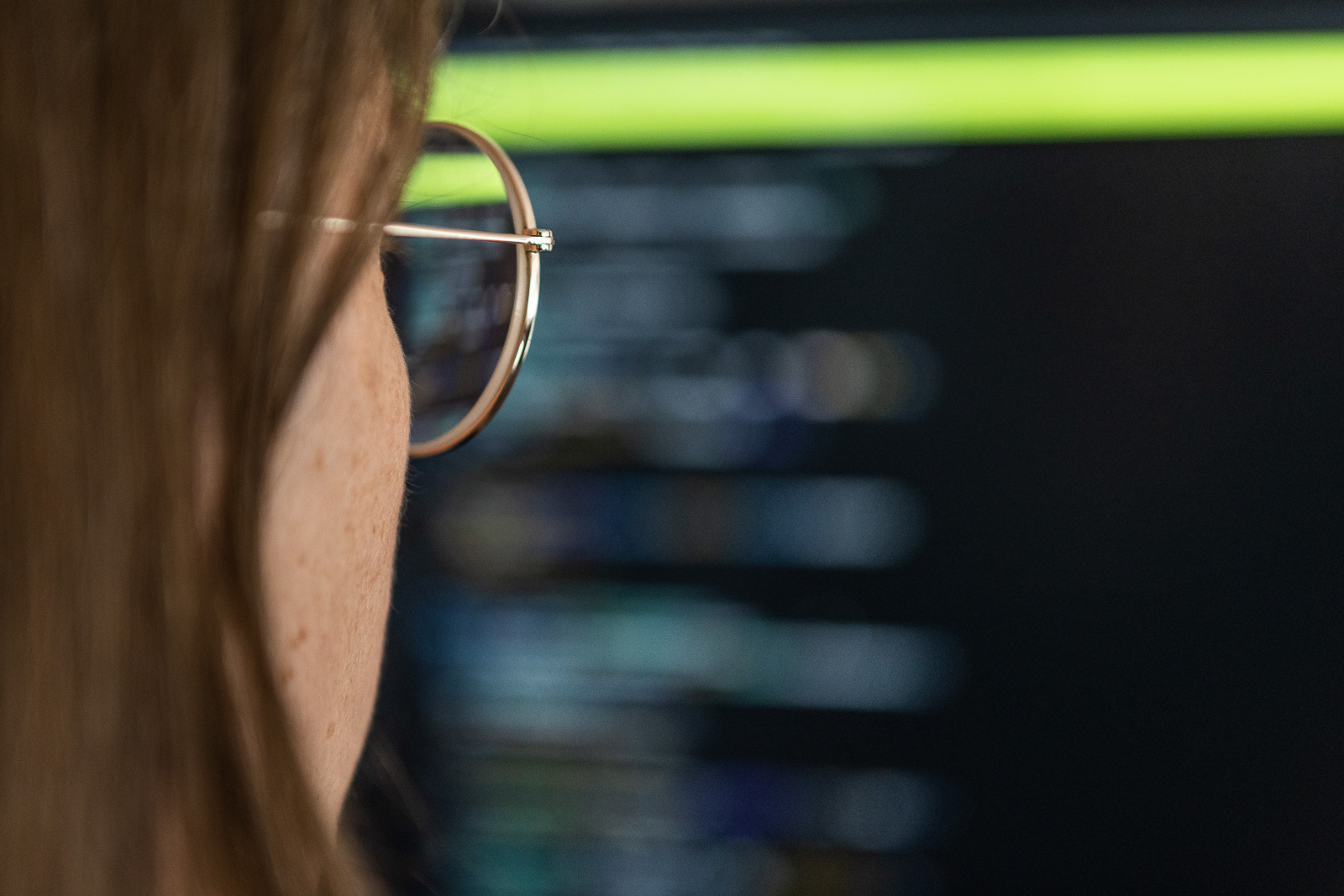 En kvinna med glasögon i förgrunden, framför en datorskärm