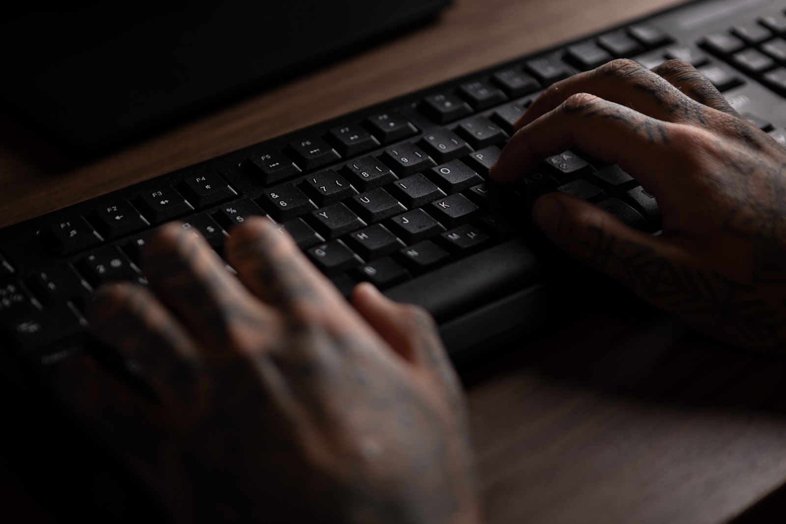Tatuerade händer på ett svart tangentbord