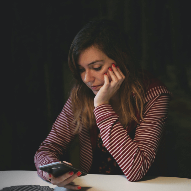 A woman in a striped long sleeved t-shirt sits by a table looking at her smartphone