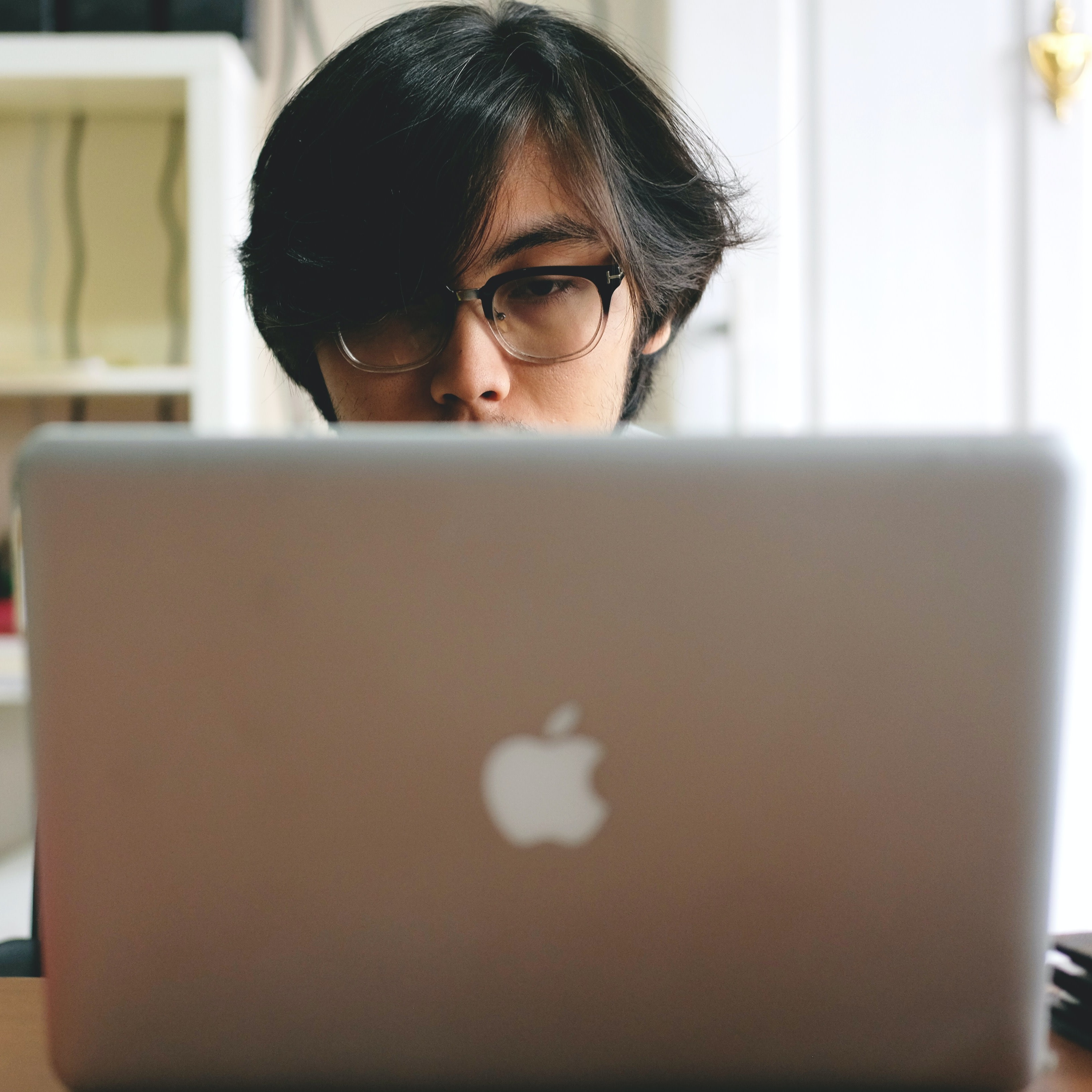 Black haired man with glasses sitting behind Apple Macbook laptop