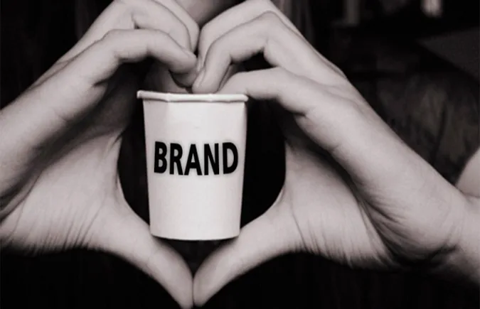 Foto: Zwei Hände, die als Herz geformt sind, halten einen Becher, auf dem das Wort „Marke“ steht.