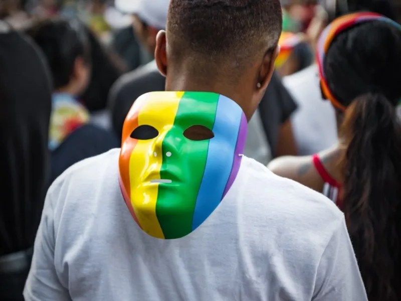 A man seen from the back with a rainbow mask