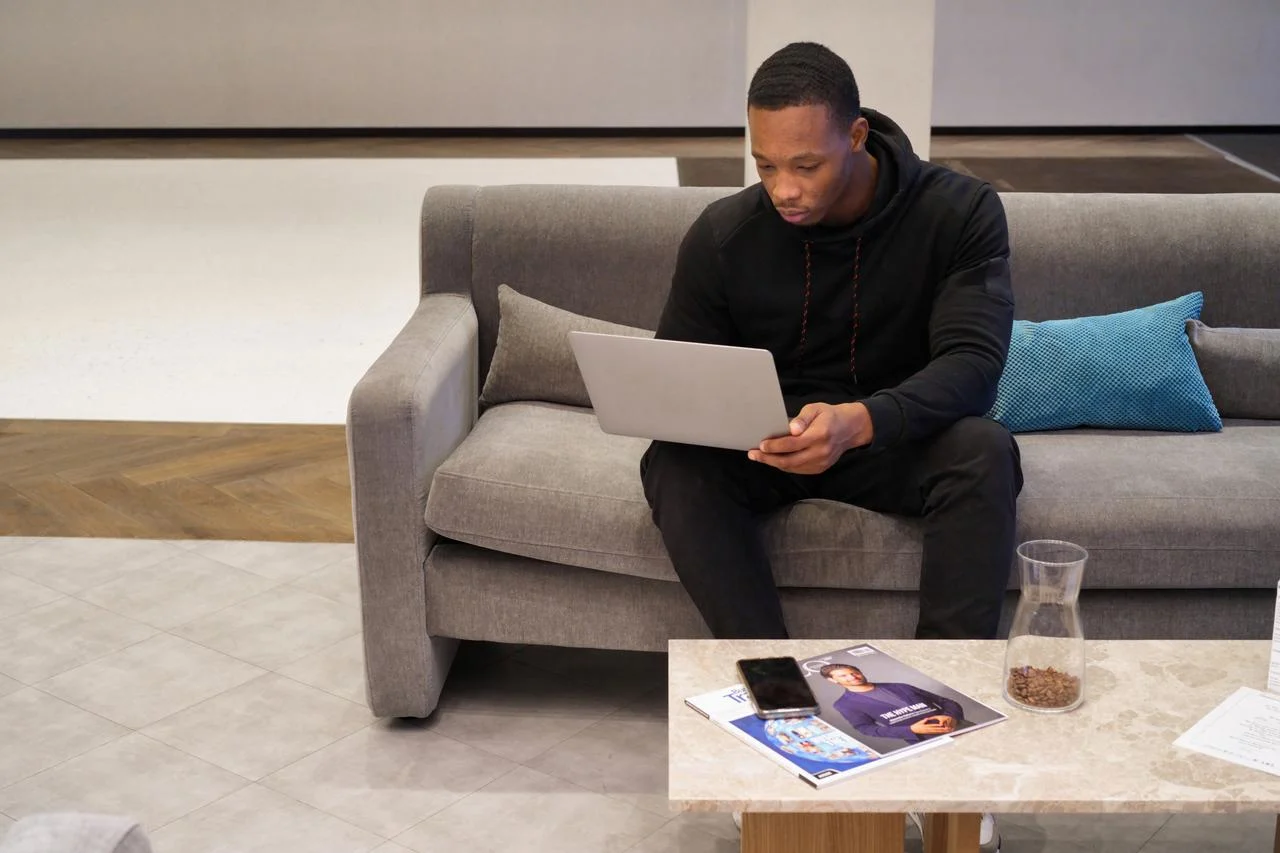 A man on a couch looking at a laptop resting on his knee Financial planning for big money moments