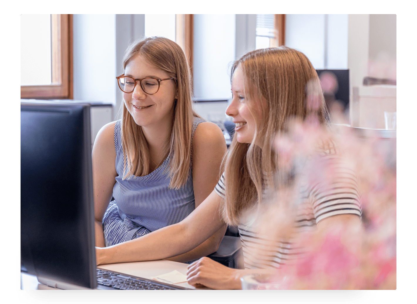 Photo of two young girls smiling and sitting in front of a computer at Trustpilot's office