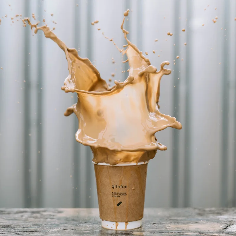 A latte coffee splashed dramatically from a brown cup standing on a marble counter top