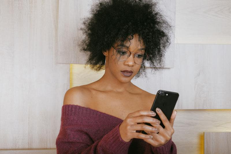 A black haired woman with glasses in a maroon dress looks at her smartphone