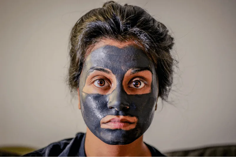 A woman with a black facial treatment looks directly into the camera