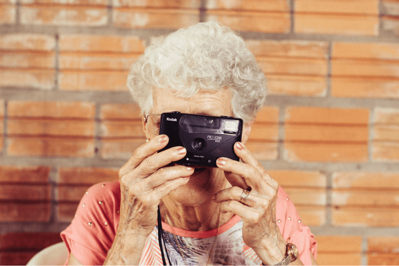 An elderly woman with white curly hair gets ready to take a photo with a camera