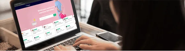 Picture of a woman typing on a laptop's keyboard while visualizing Trustpilot's homepage