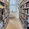 An image of a library looking down a long row of books. There is a white chair and table at the end of the row. Trustpilot Pride & Allies Resources