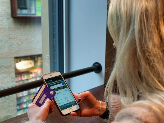 A woman is sitting on a stool holding her phone and bank card A beginner's guide to smart investing