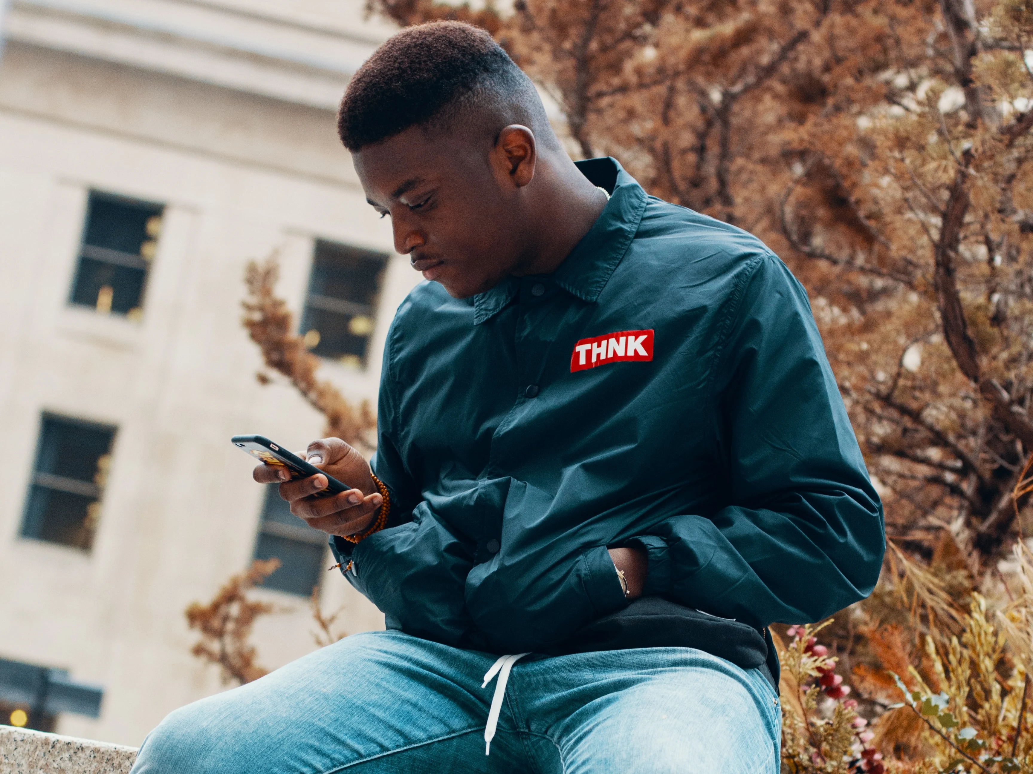 Young man sitting on a park bench looking at his smartphone with a tree in the background Common phone scams