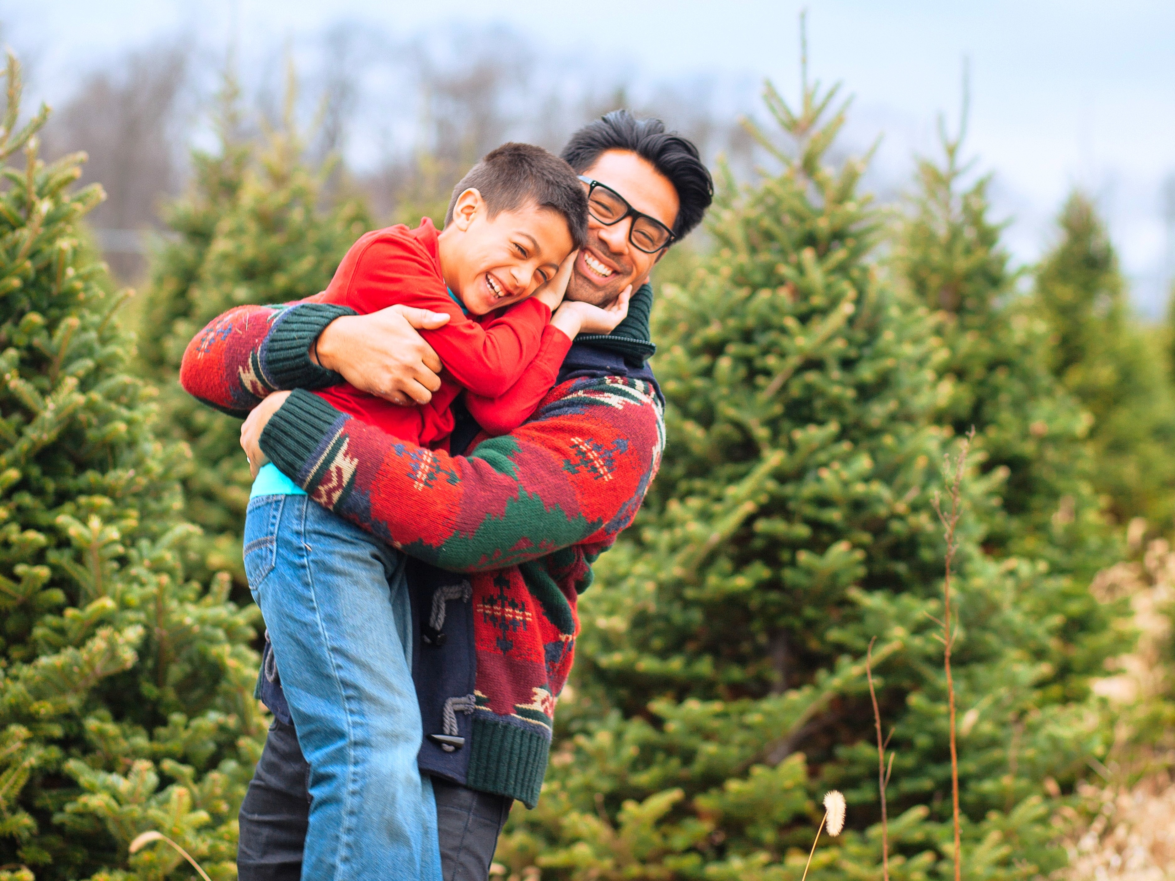 Dad hugging his son in front of a group of Christmas trees