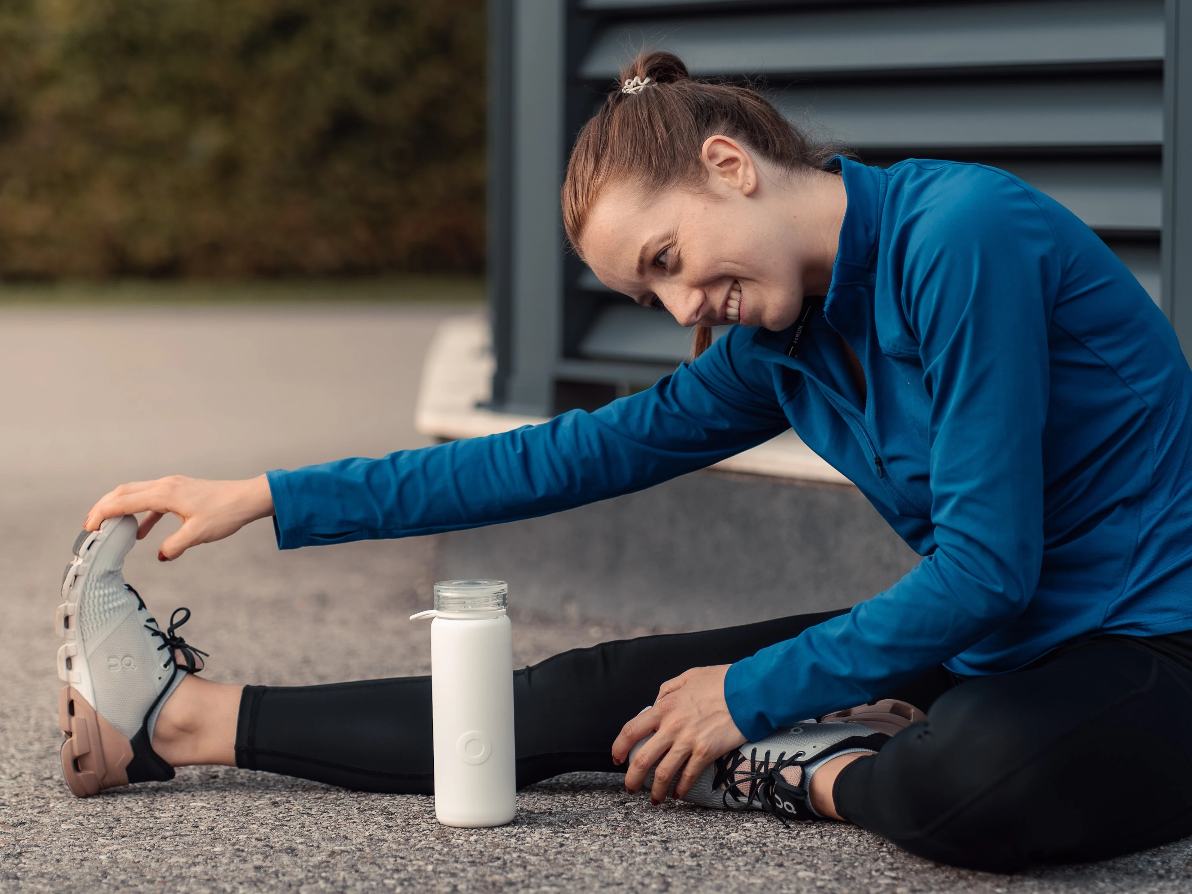 Woman wearing a blue top and yoga pants sitting and stretching her legs. A white water bottle is in front of her. Build a healthier daily routine with these 8 wellness products