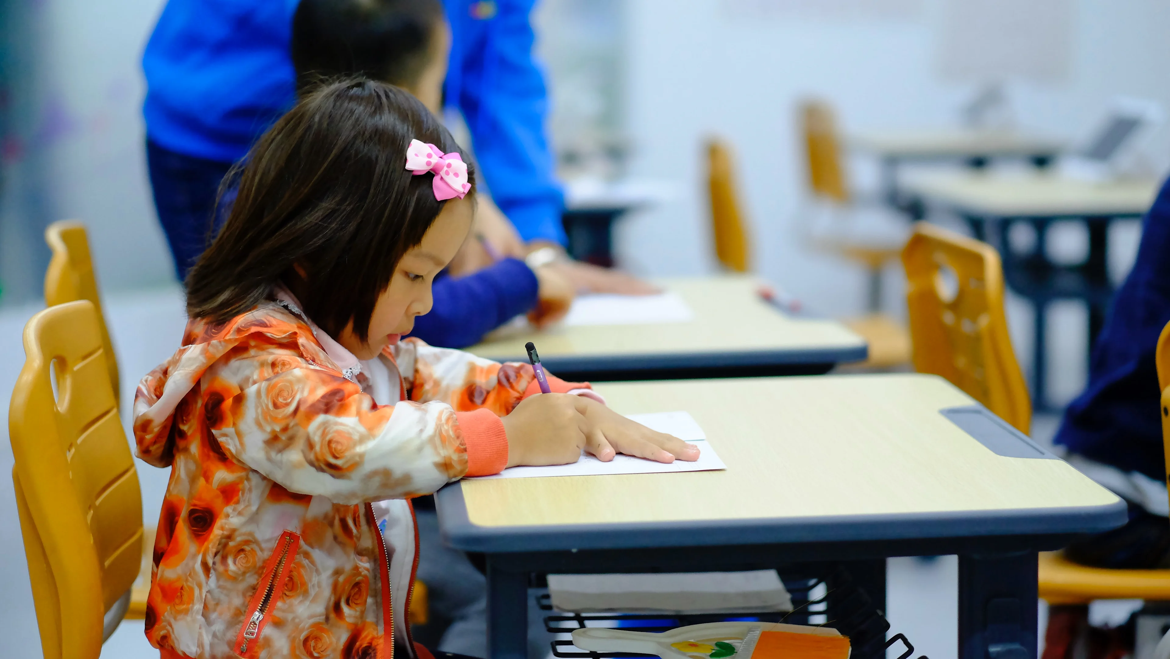 What consumers have revealed about back-to-school season in their reviews Young girl sits on a yellow school chair by a school table writing on a piece of paper