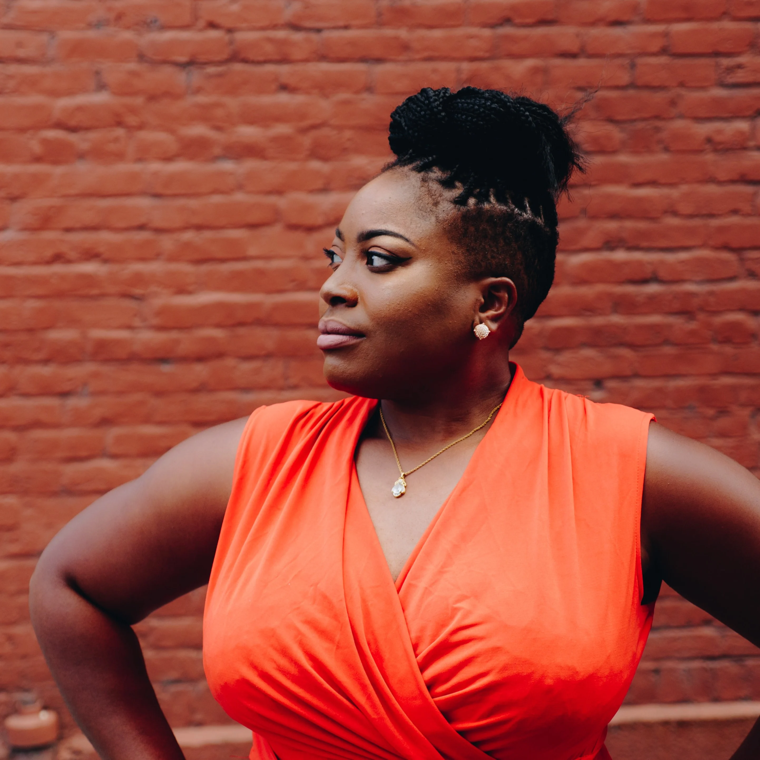 Black woman in orange dress standing in front of brick wall