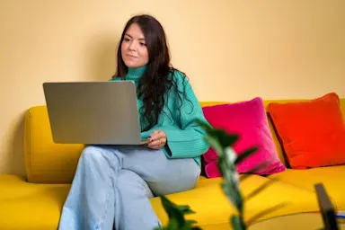 A woman sitting on a couch looking at her laptop Romance scams