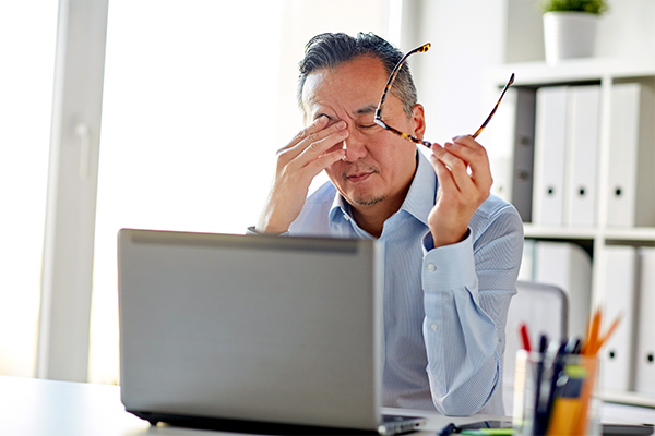 Man behind laptop rubbing eyes