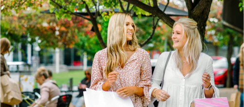 Two women carrying bags talking outdoors