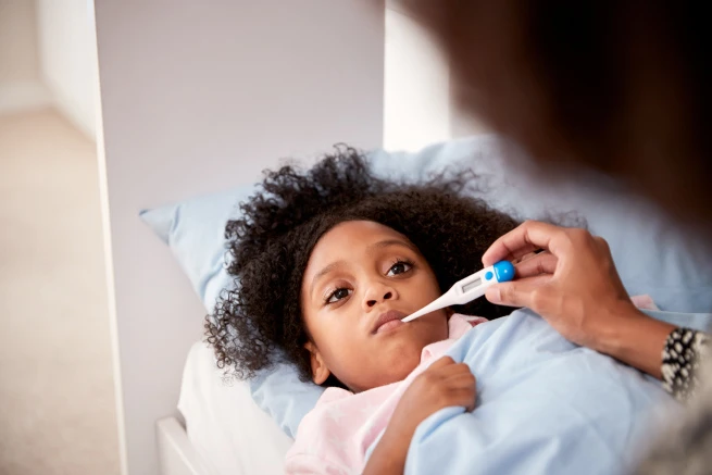 Child laying in bed with a thermometer
