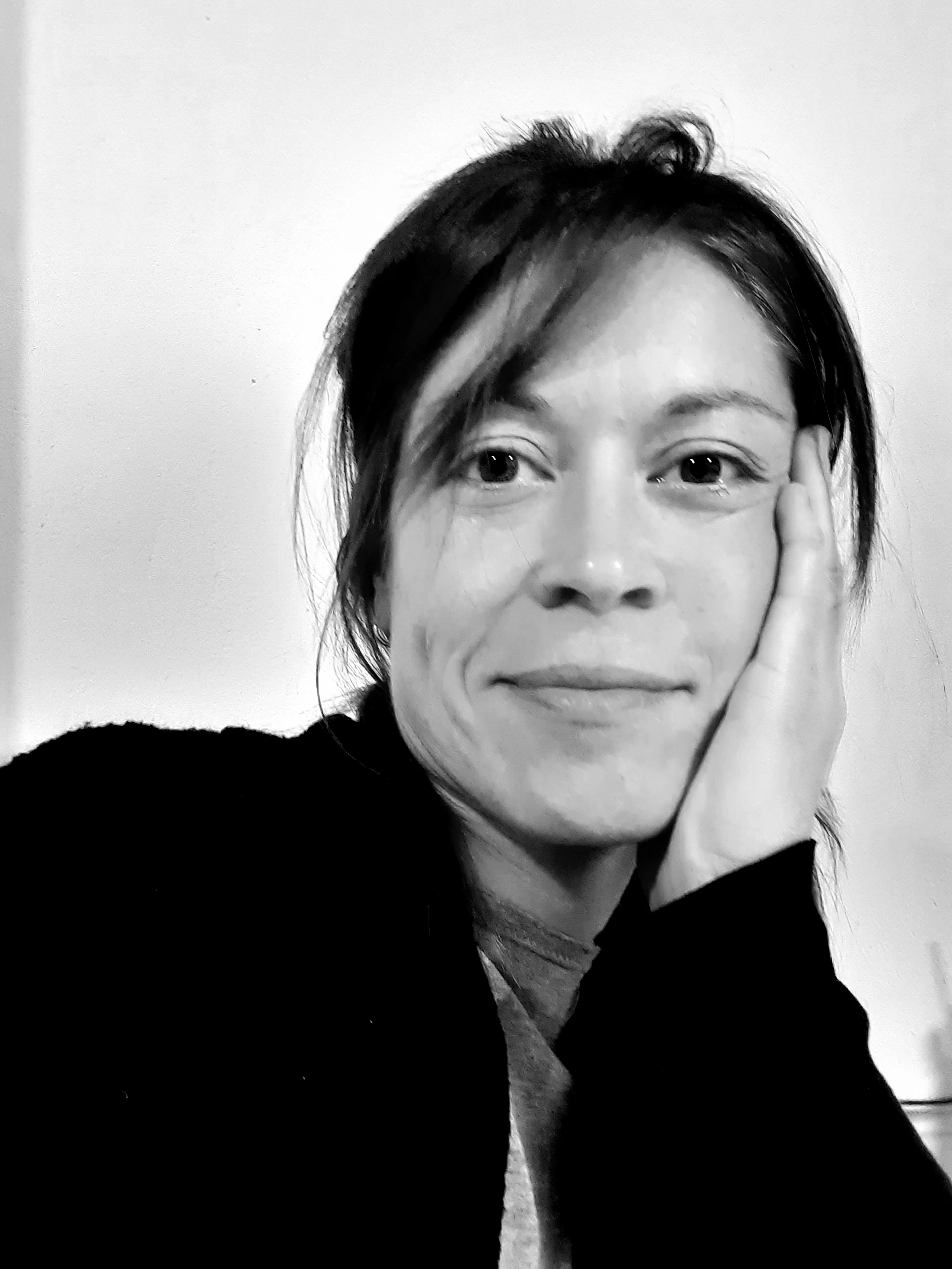 Imatge de perfil d'Iris Hinojosa en blanc i negre on surt somrient amb el cap recolzat a la mà 