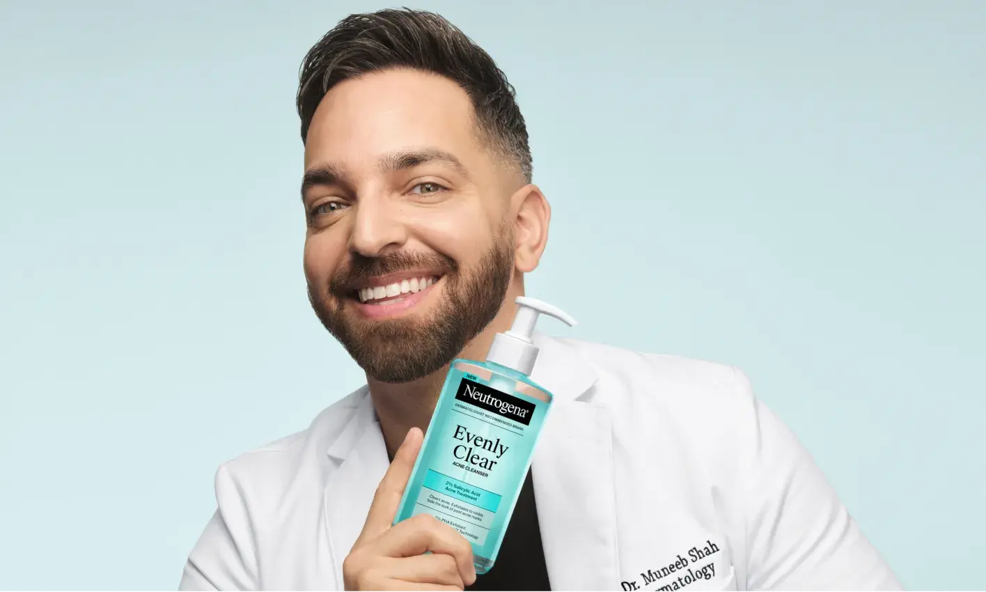 Doctor Muneeb Shah, Dermatologist, holding a bottle of Evenly Clear™ Acne Cleanser