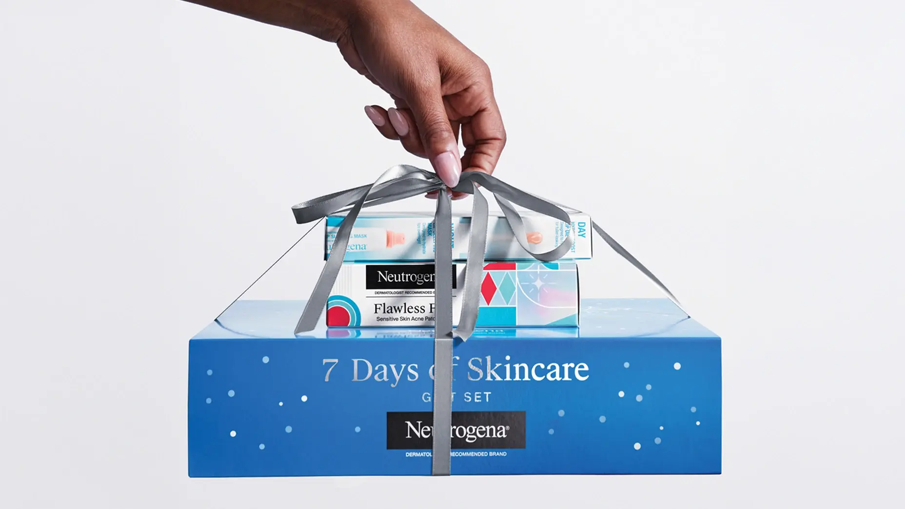 A hand holds a silver ribbon tied around a stack of Neutrogena products, featuring a large blue box labeled "7 Days of Skincare Gift Set.