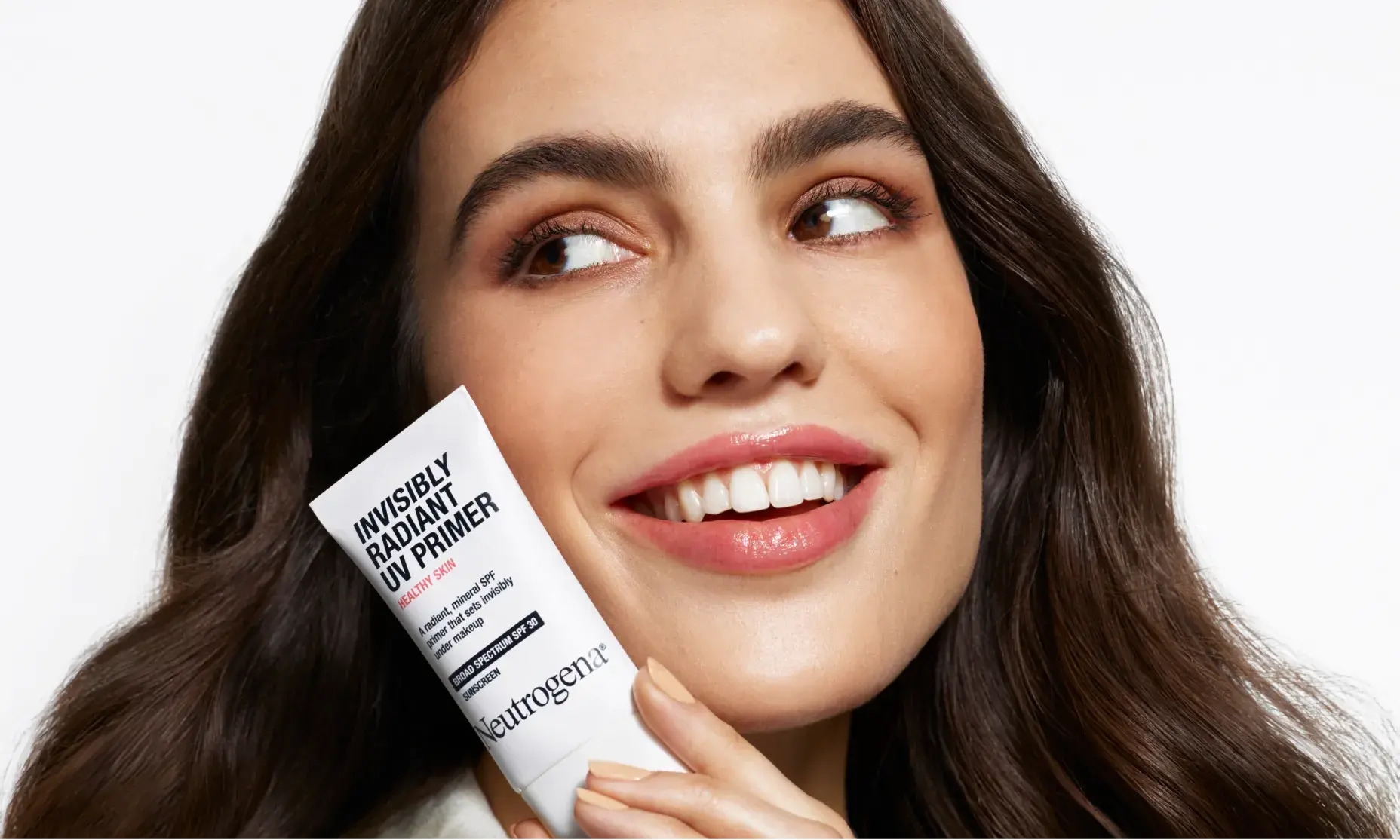Smiling woman holding a tube of Neutrogena Invisibly Radiant UV Primer near her face.