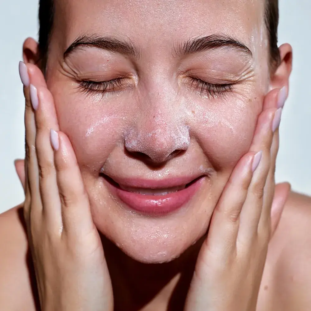 Young woman applying white foam cosmetic product to her face.