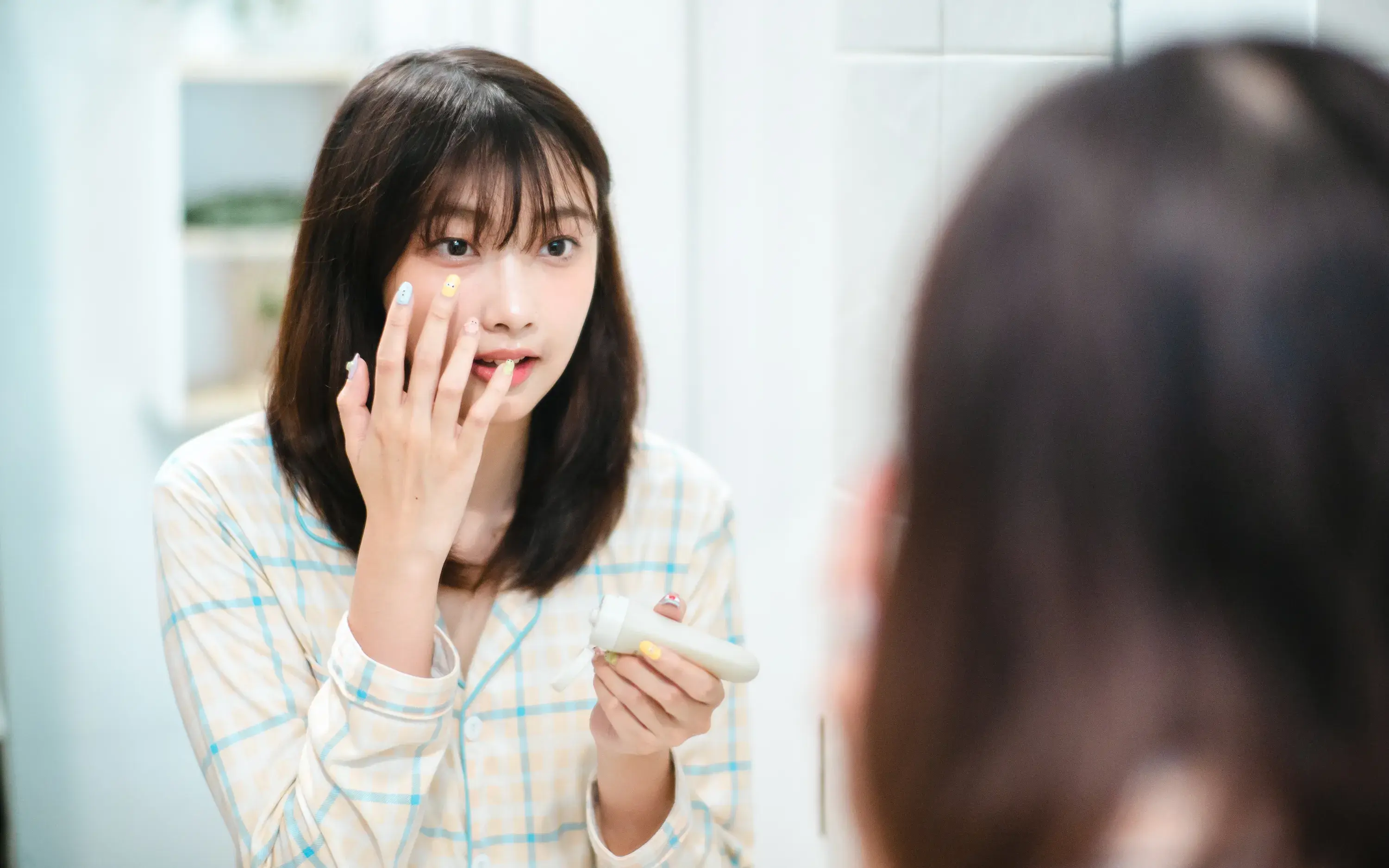 A woman applies cream to her face in the mirror.