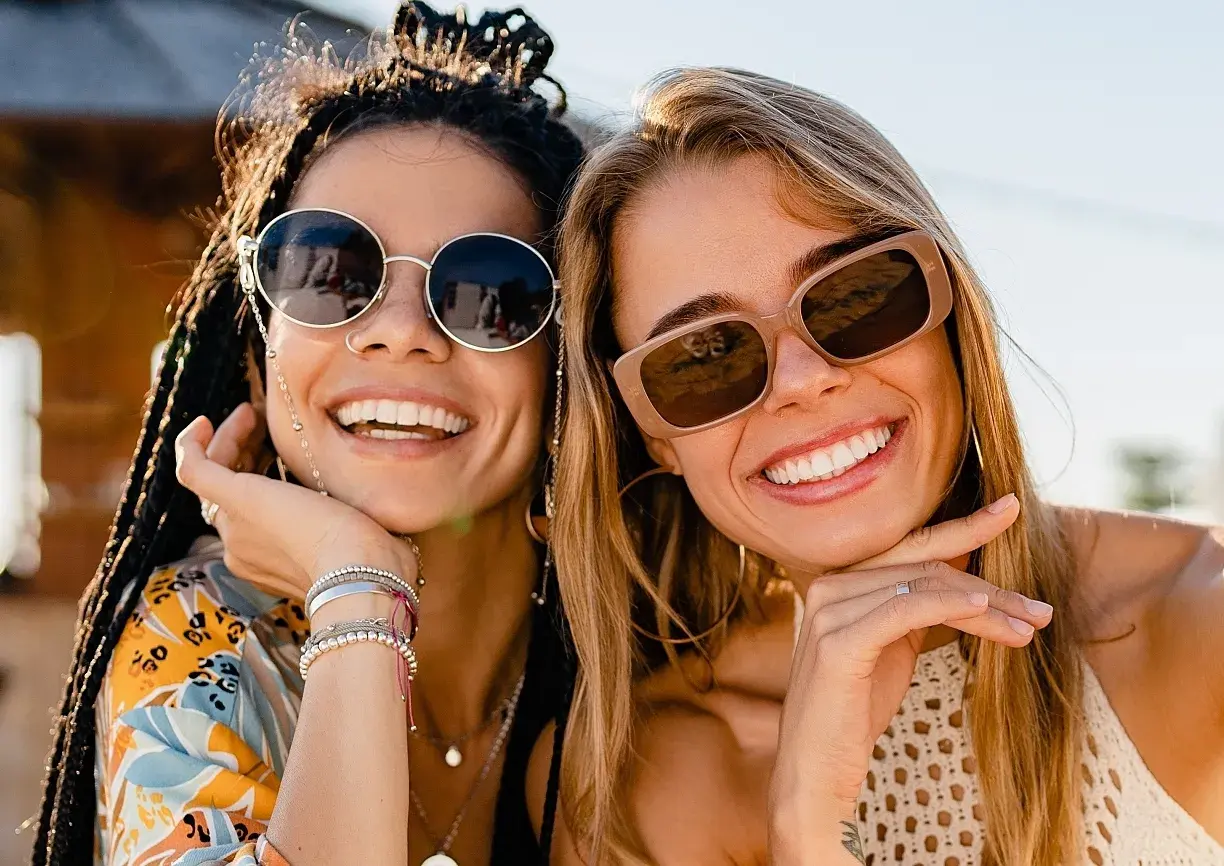 Two women wearing sunglasses smile for a selfie. 