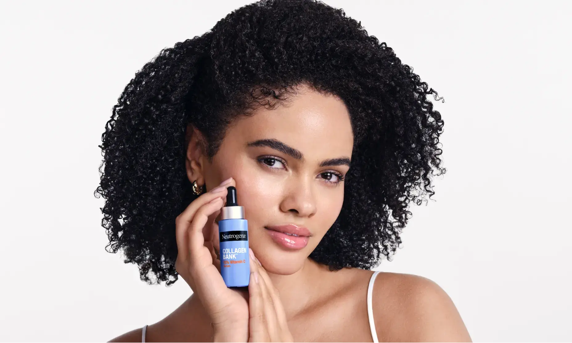 Woman with curly hair holding Neutrogena® Collagen Bank 15% Vitamin C Glow Serum
