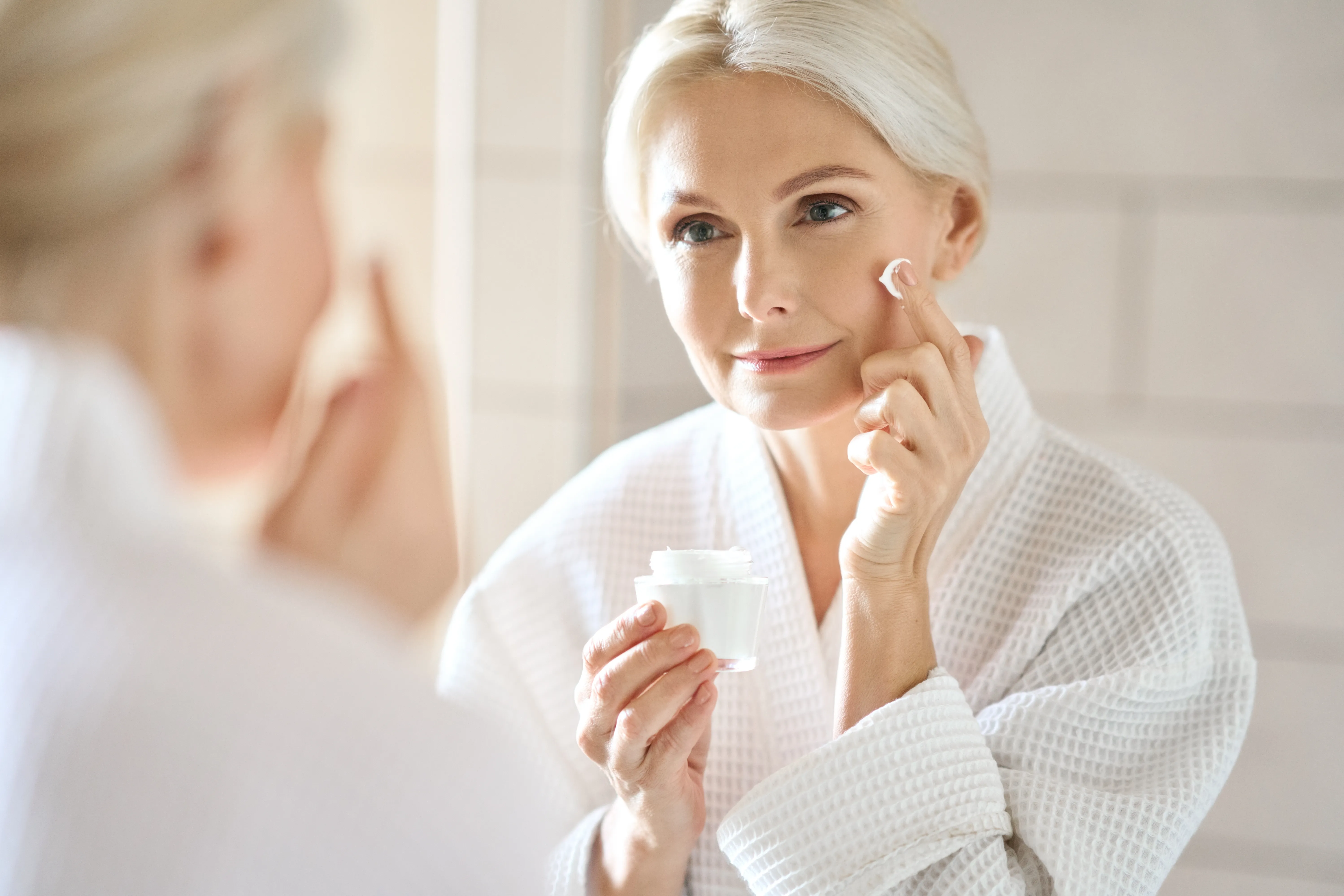 A woman applies cream to her face.