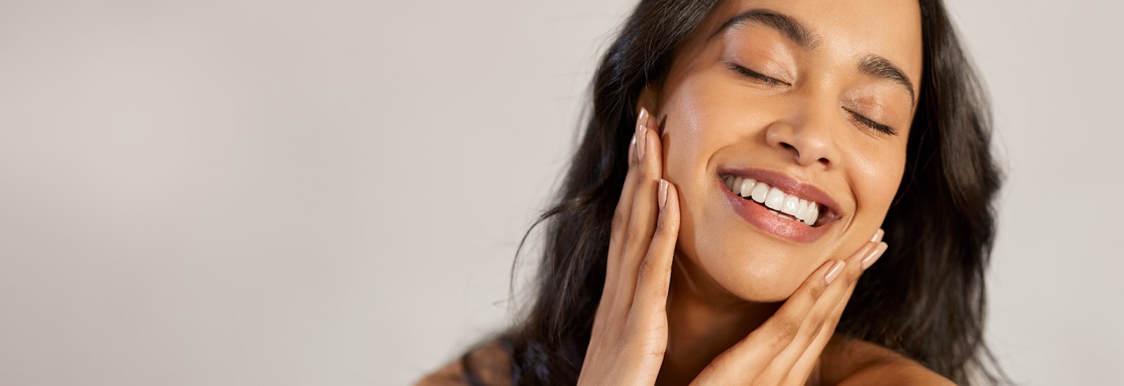 A woman smiles with her hands on either side of her face.