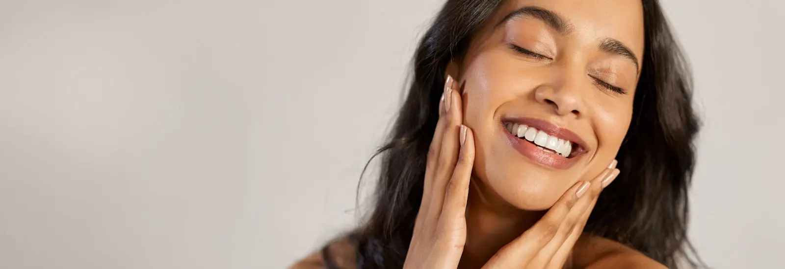 A woman smiles with her hands on either side of her face.