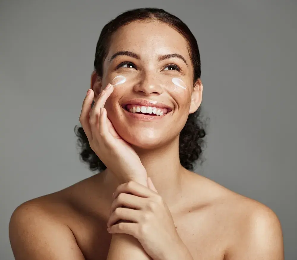 A woman holds a dropper up to her cheek.