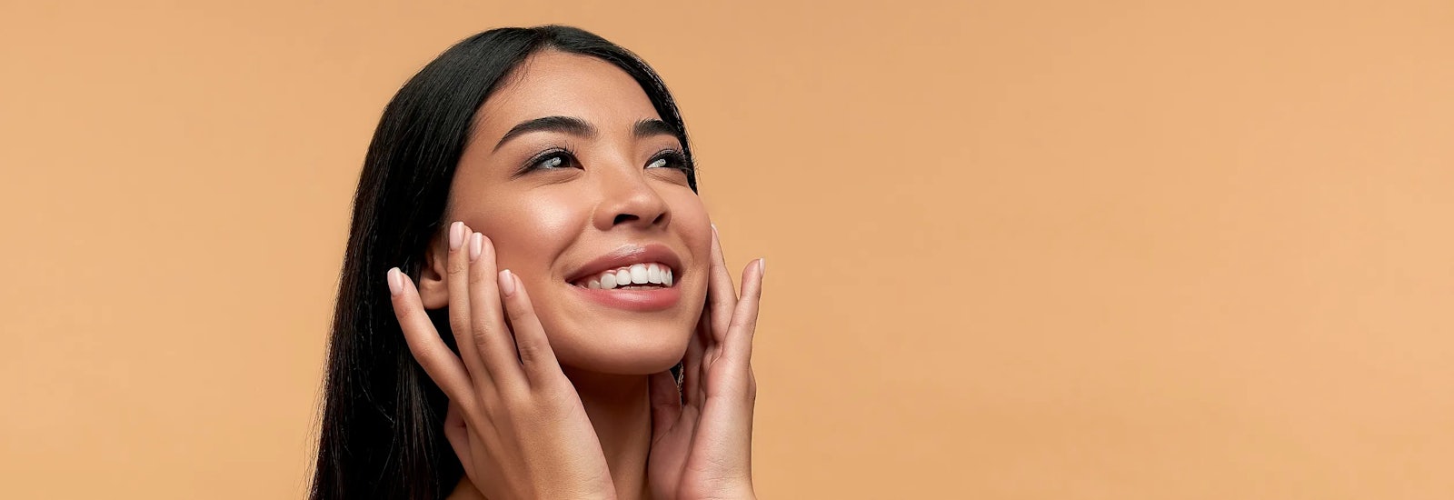 A smiling woman touches either side of her face with her fingertips.